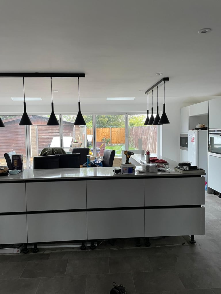 Modern kitchen with gray cabinetry, black pendant lights, and large windows overlooking a brick patio